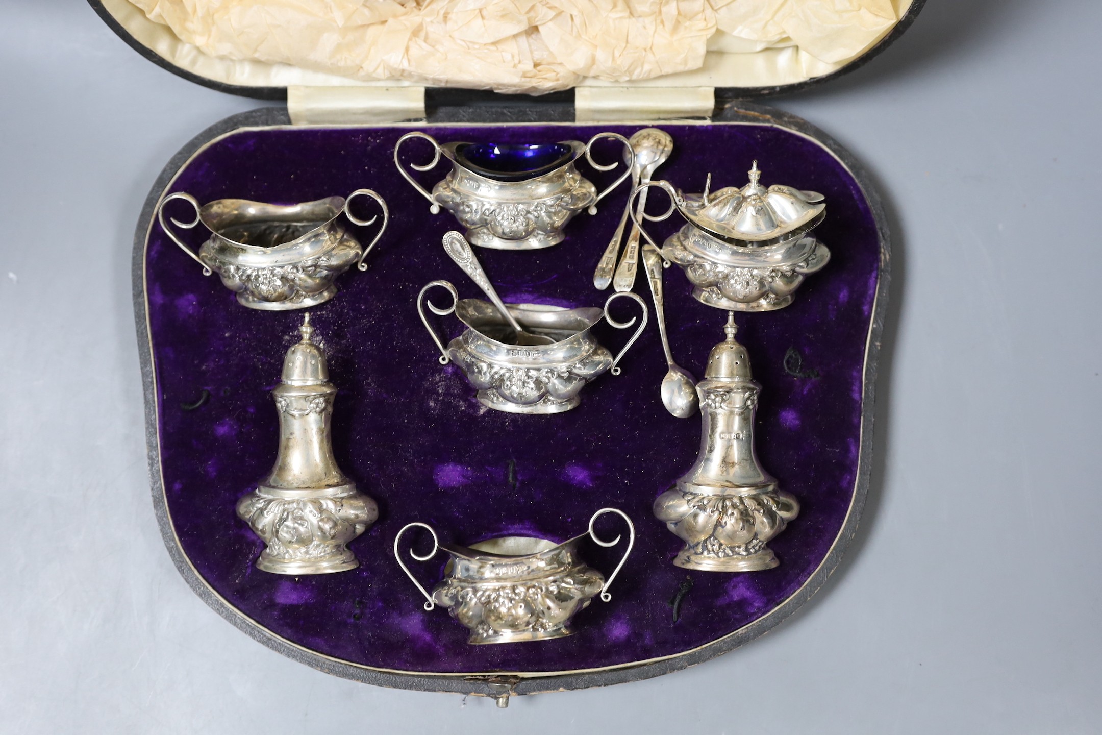 A late Victorian embossed silver six piece condiment set, together with four spoon, Sheffield, 1901, by Walker and Hall.